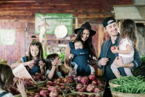 woman holding baby in Ergobaby carrier while shopping at the market with young family