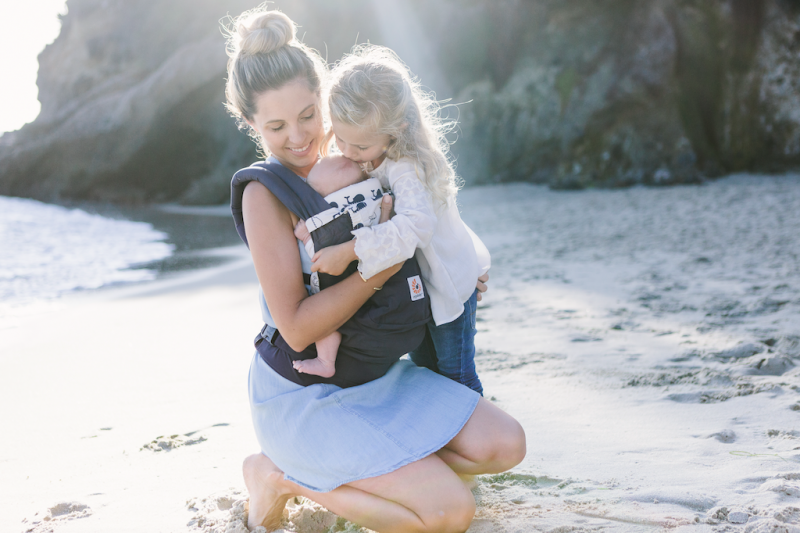 woman holding baby in original ergobaby carrier on beach