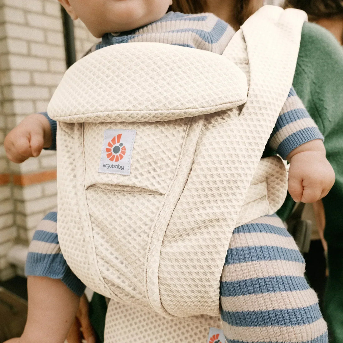 Baby being carried in a white mesh baby carrier