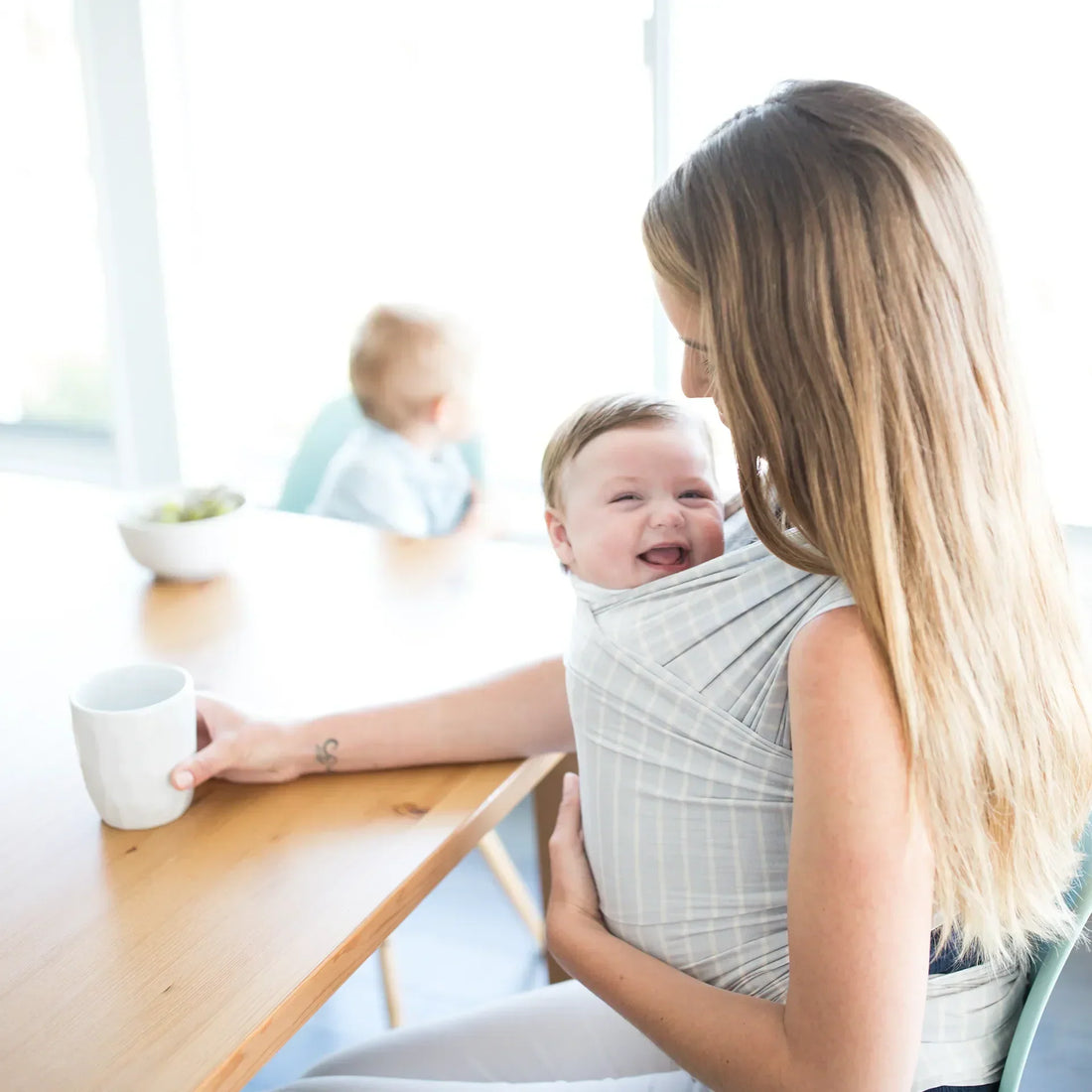 Woman holding a baby in a grey striped baby wrap while sitting at a table