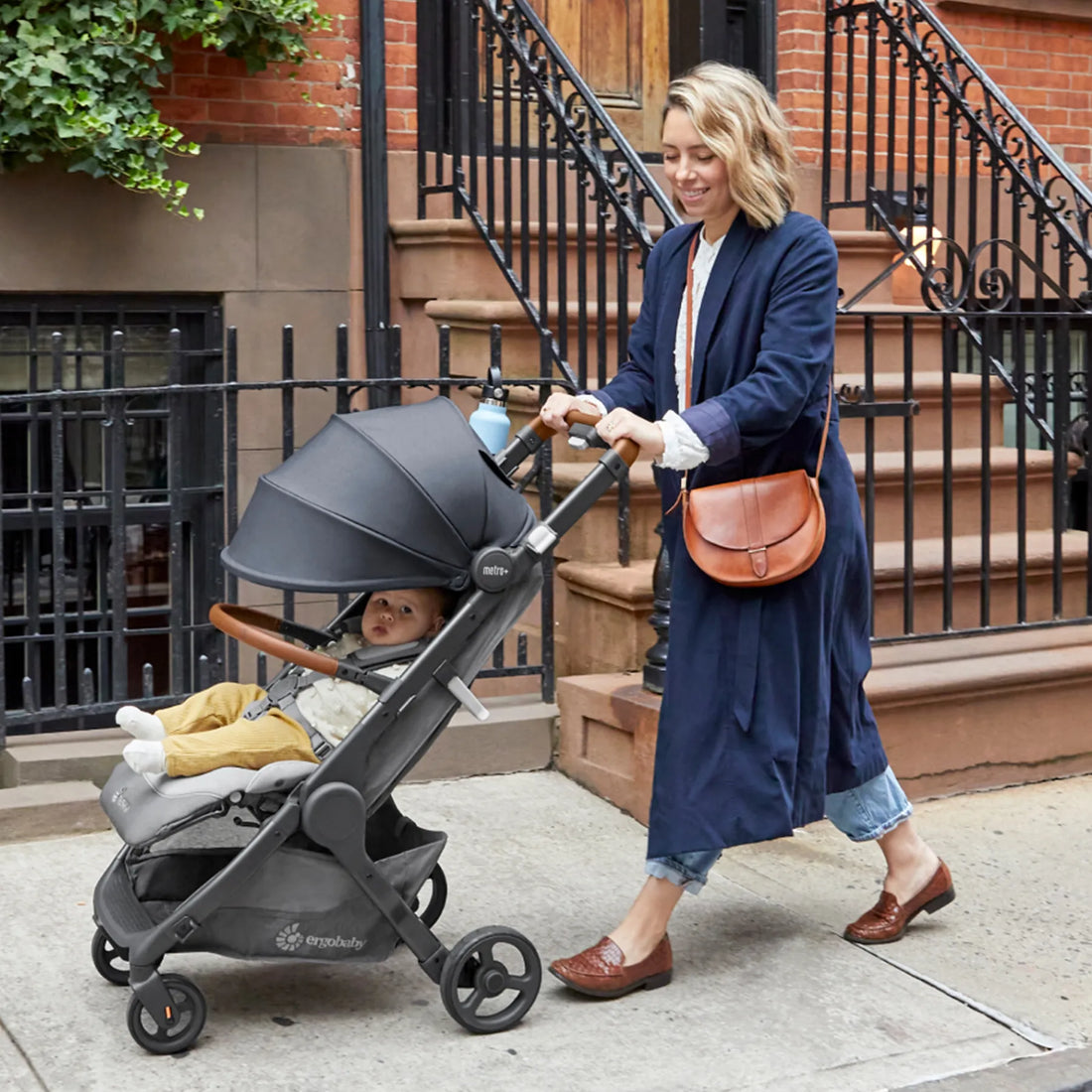 Woman in a coat pushing a baby in a stroller down the street 