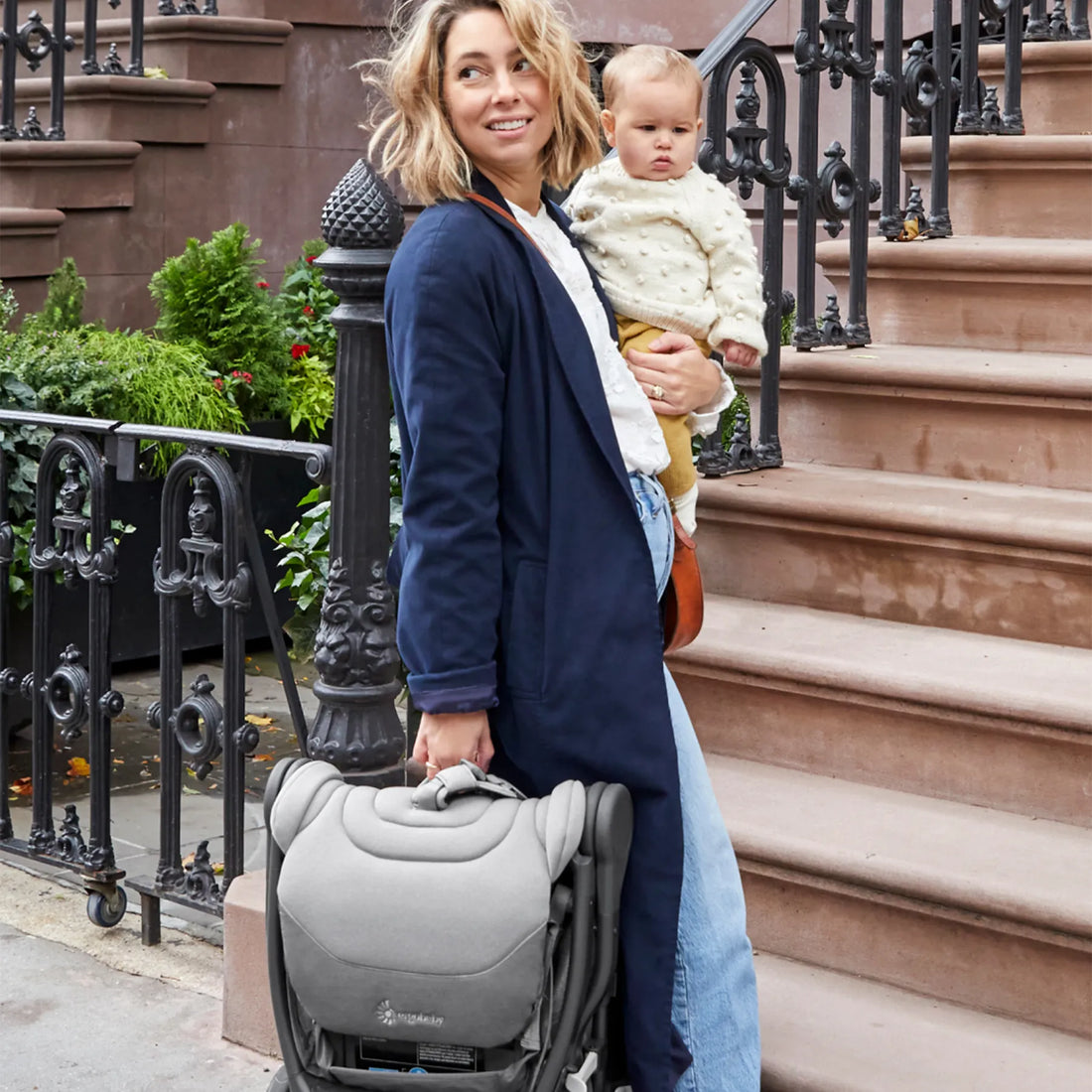 Woman holding a baby on her hip and a travel stroller 
