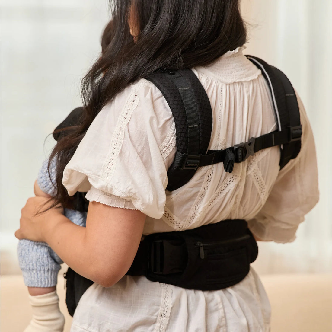 Back of person wearing a black baby carrier holding a baby 