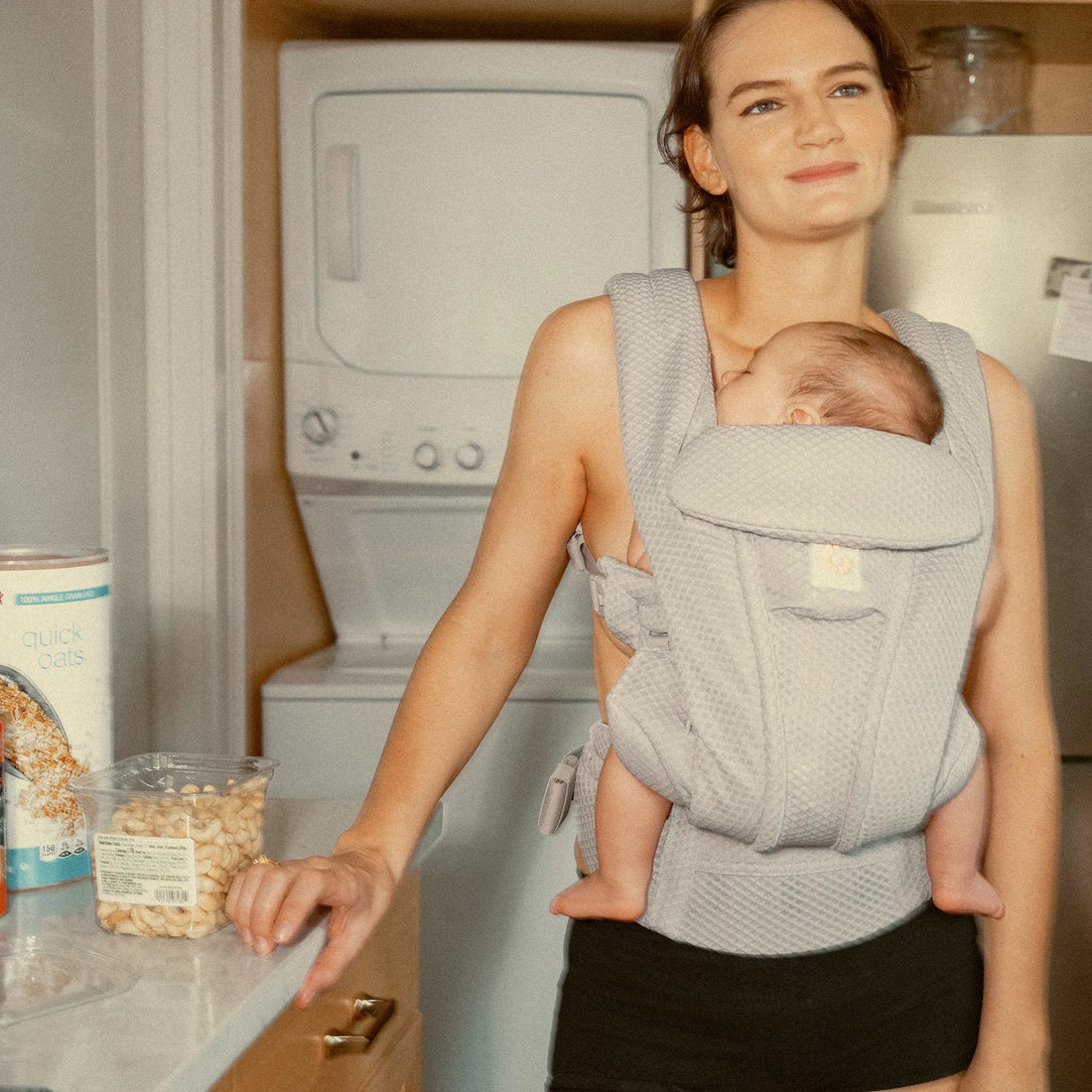 Woman holding a baby in a grey baby carrier