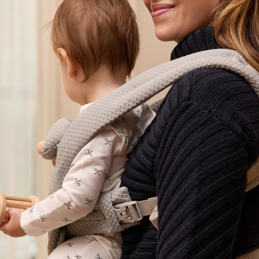 Woman holding a baby in a gray baby carrier with the baby facing out