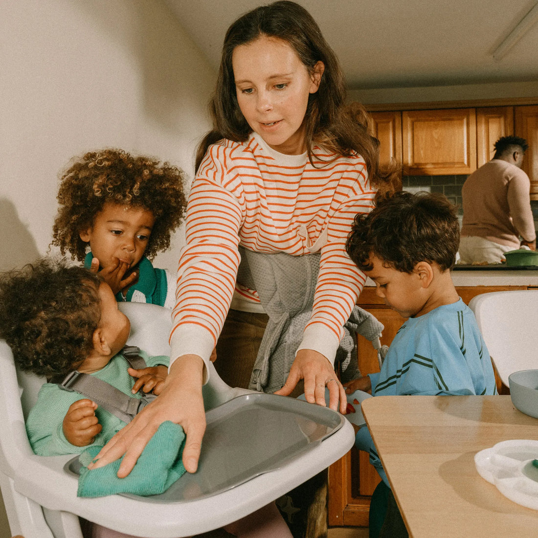 Woman cleaning a high chair with two toddlers next to her