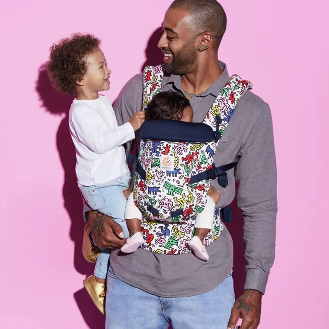 Man holding a baby on his hip and a baby in a printed baby carrier