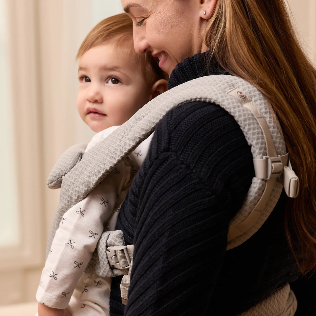 Woman holding a baby a light grey baby carrier with baby facing out