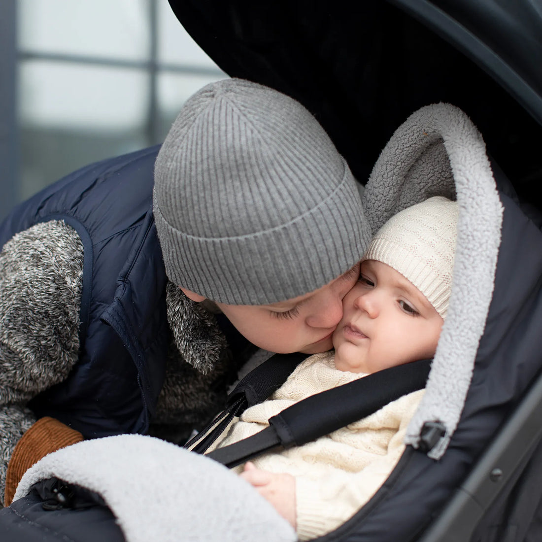 Kid leaning down to kiss baby in a stroller 