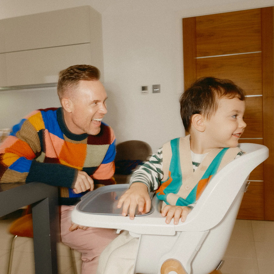 Man sitting at a table with a baby in a high chair laughing