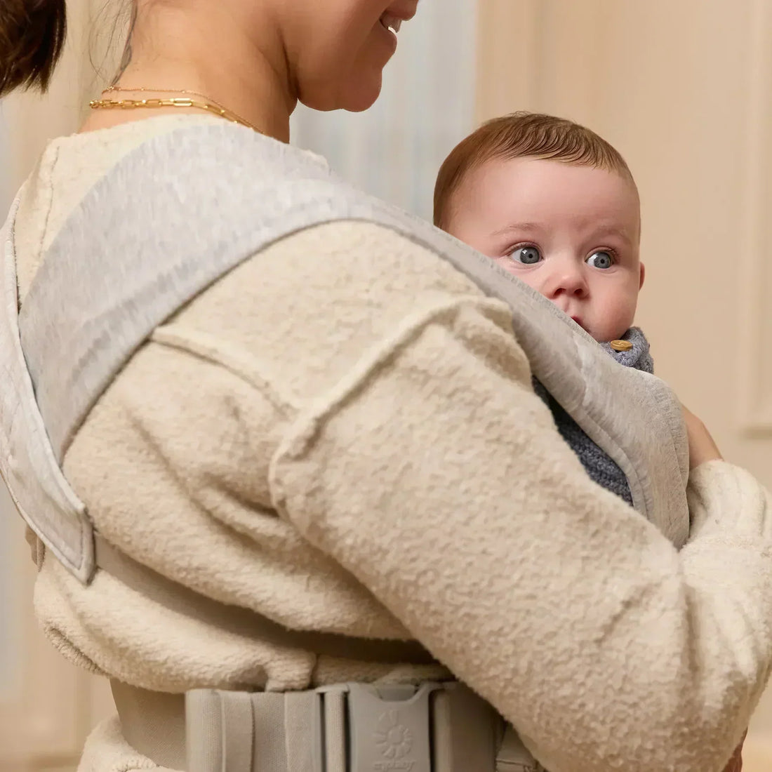 Woman holding baby in a light grey baby carrier