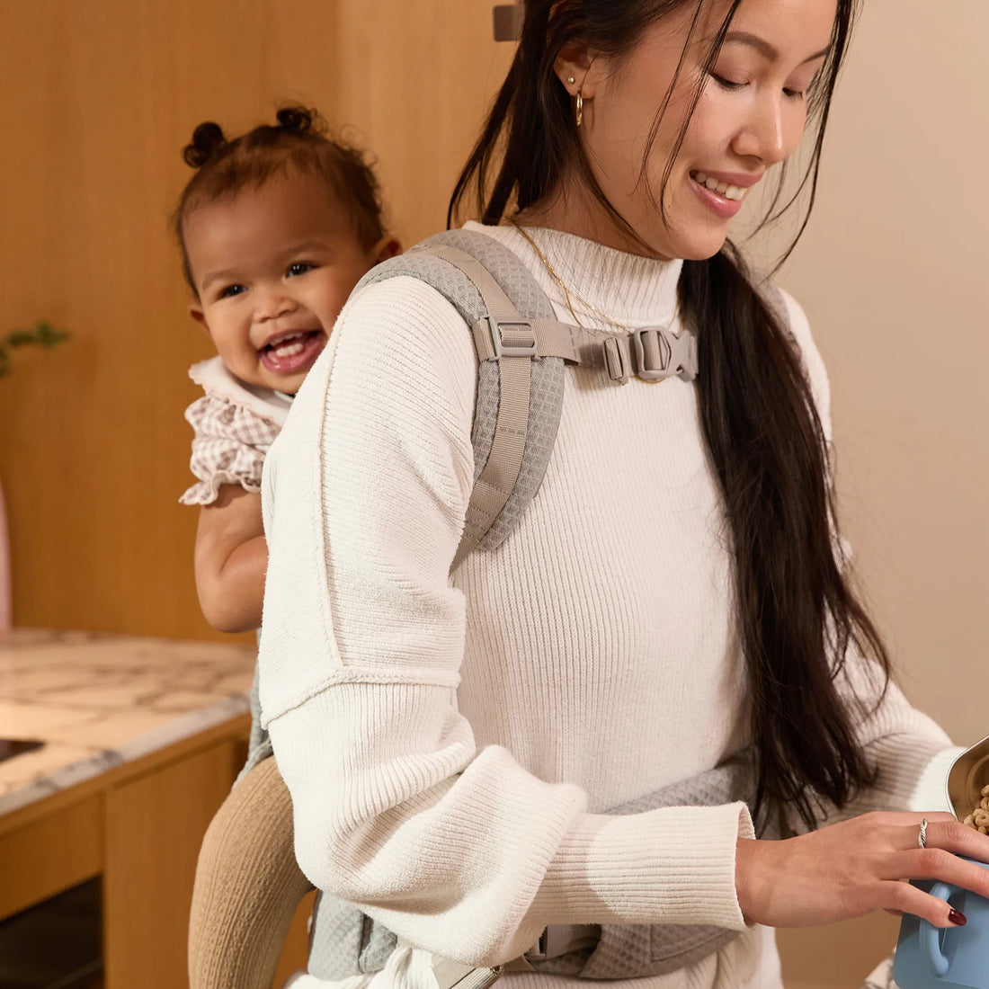 Woman wearing aa grey baby carrier with baby on her back