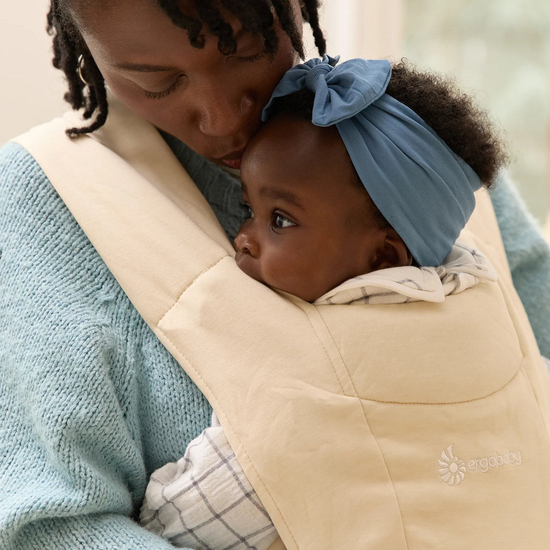 Woman holding a baby in a beige baby carrier