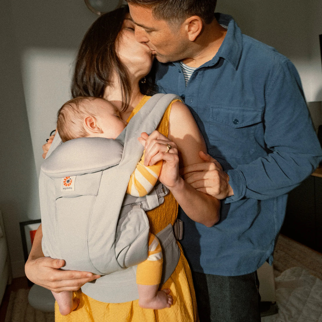 Woman holding a baby in a baby carrier kissing a man