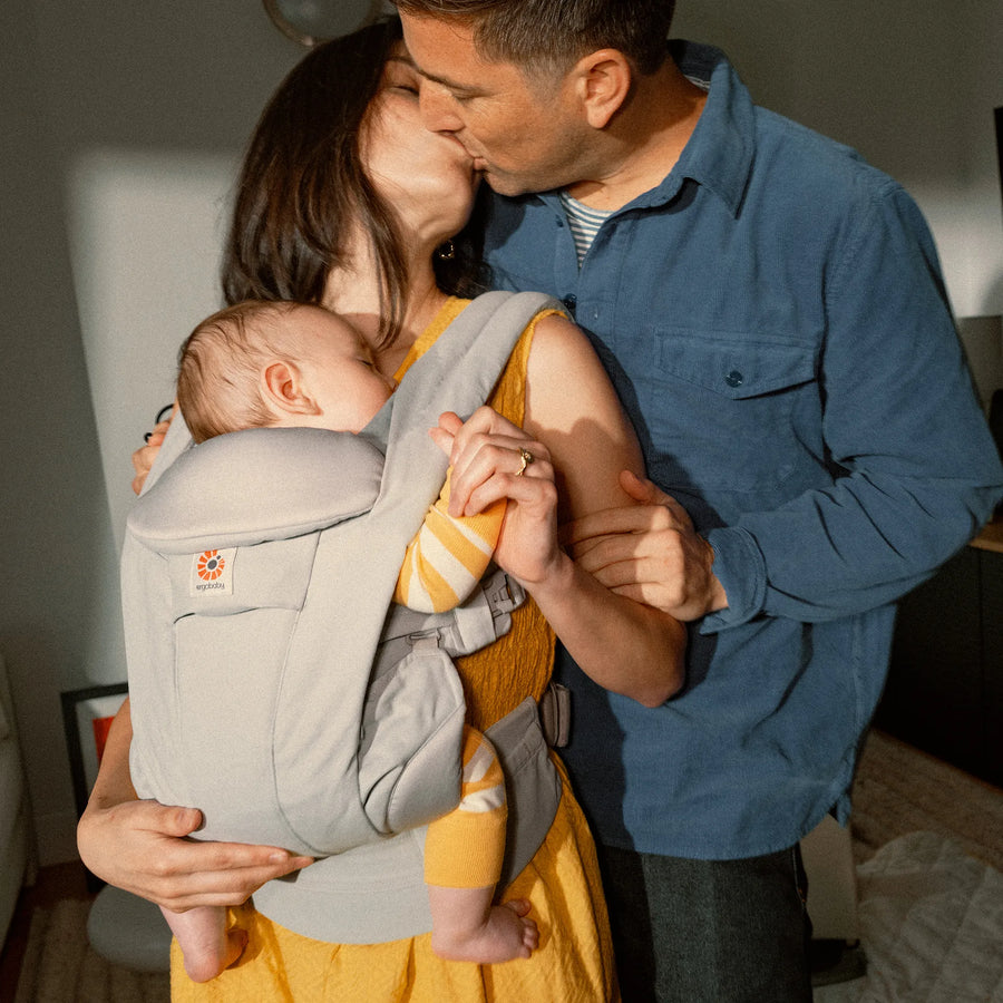Woman holding a baby in a baby carrier kissing a man