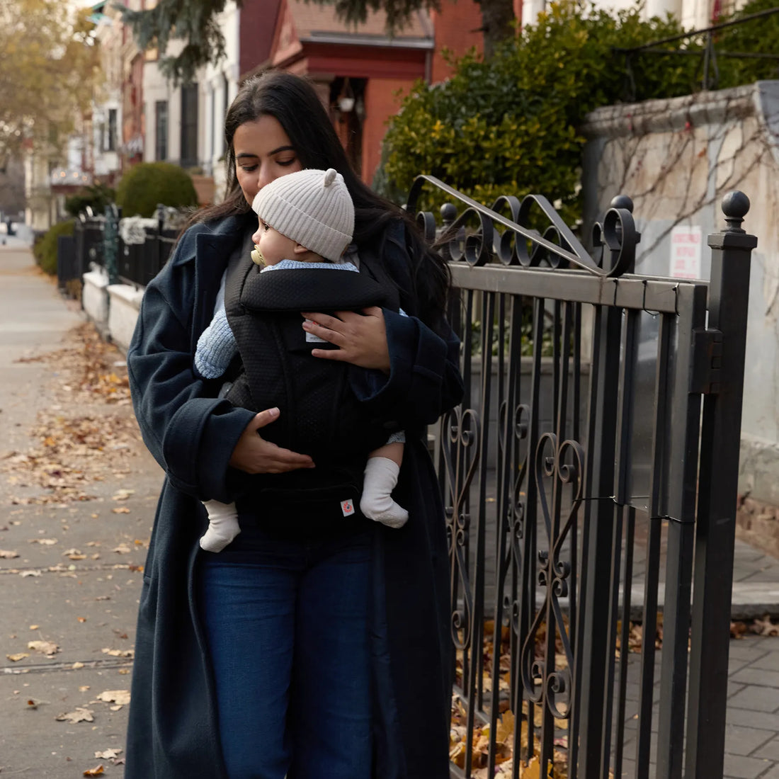 Woman in a coat holding a baby in a black baby carrier