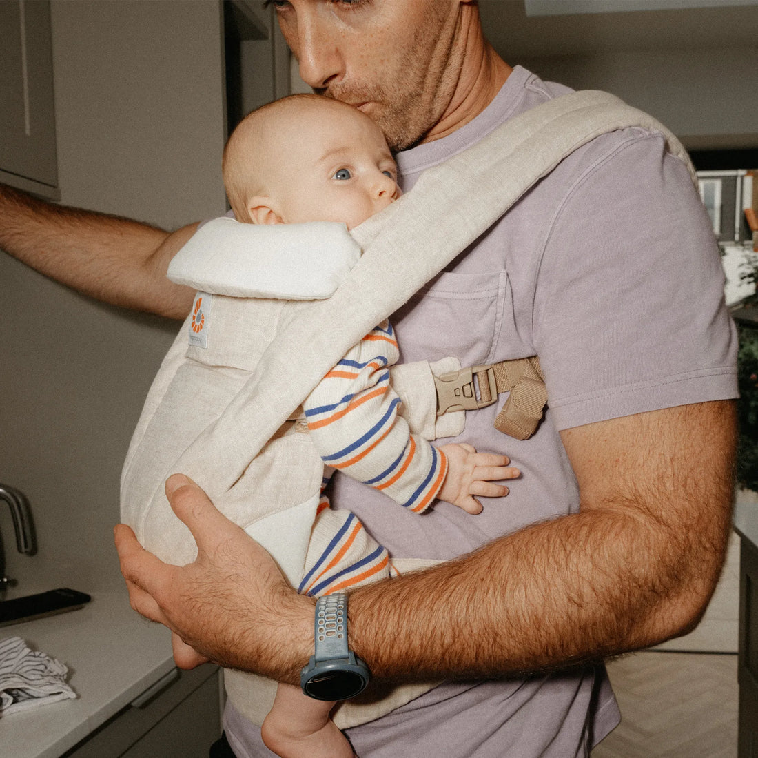 Man holding a baby in a beige baby carrier