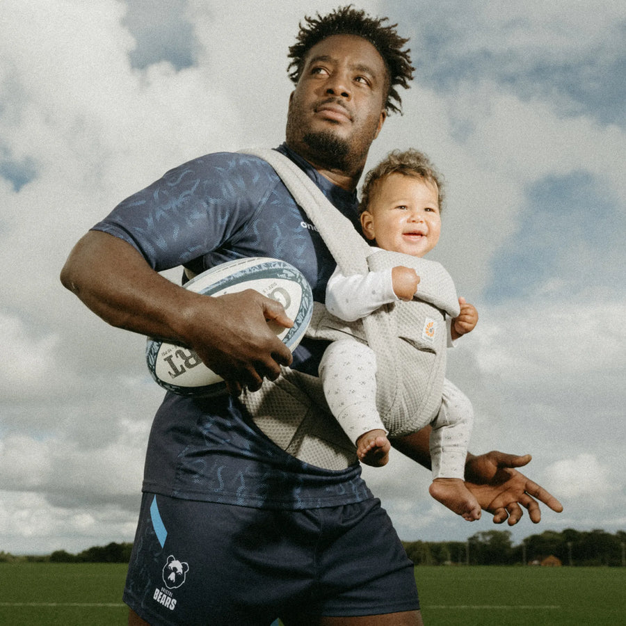 Man holding a baby in a grey baby carrier and a football