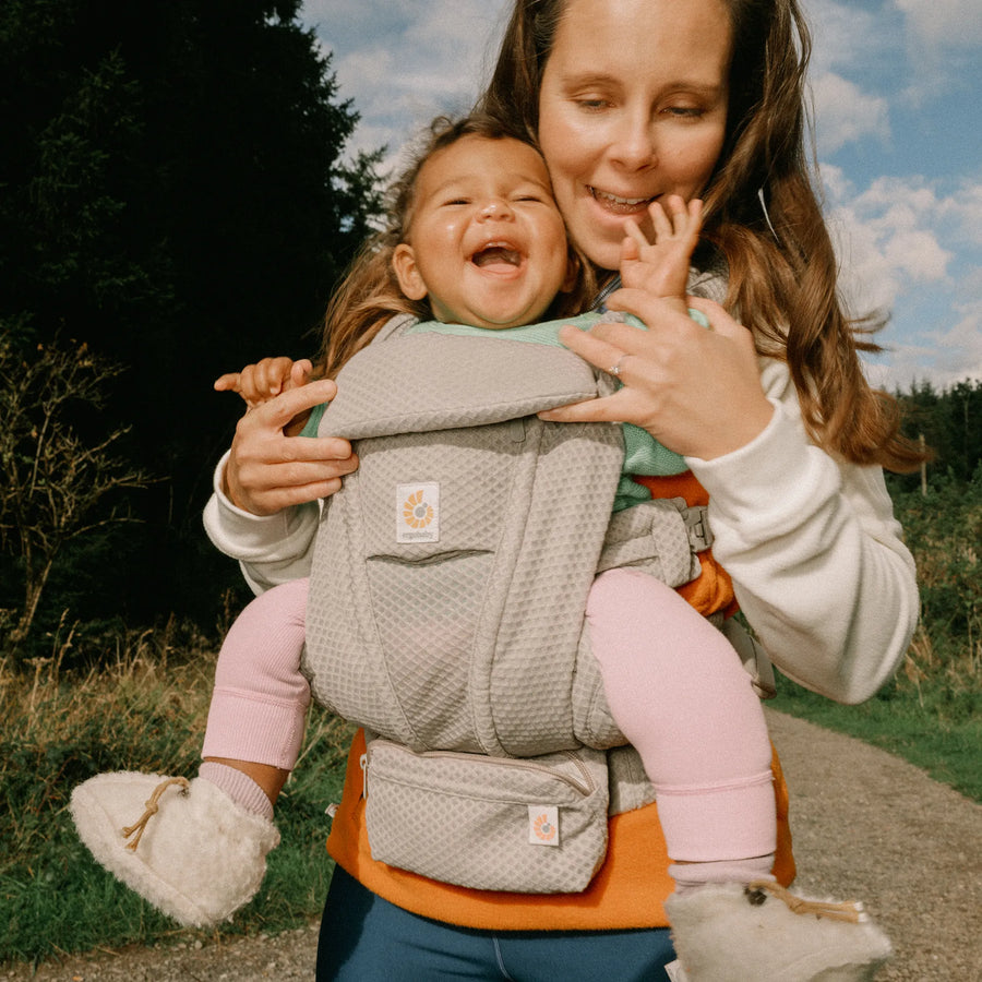 Woman holding baby in a grey baby carrier