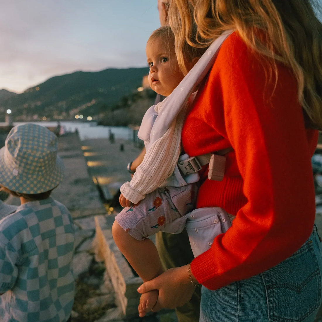 Woman holding a baby facing out in a baby carrier outside