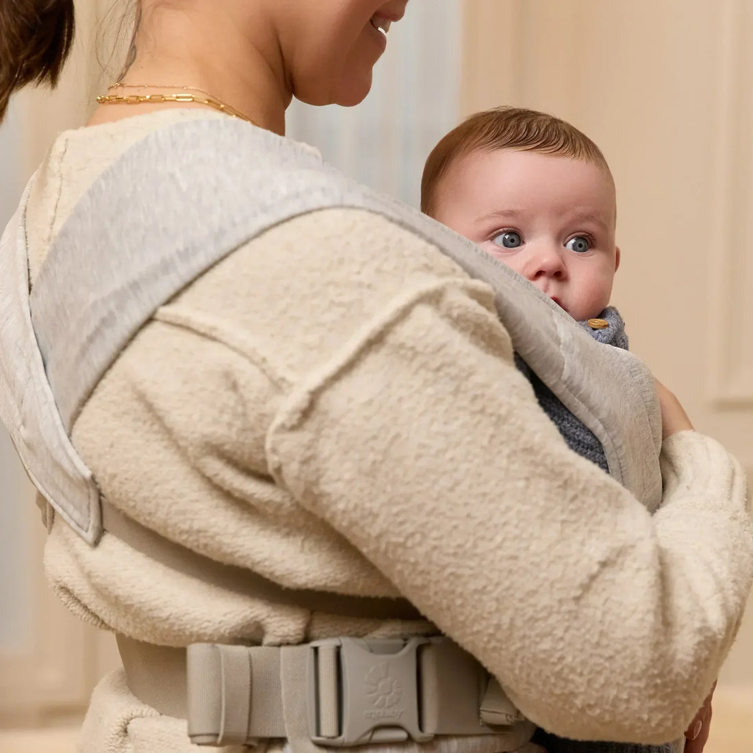 Woman holding a baby in a grey baby carrier