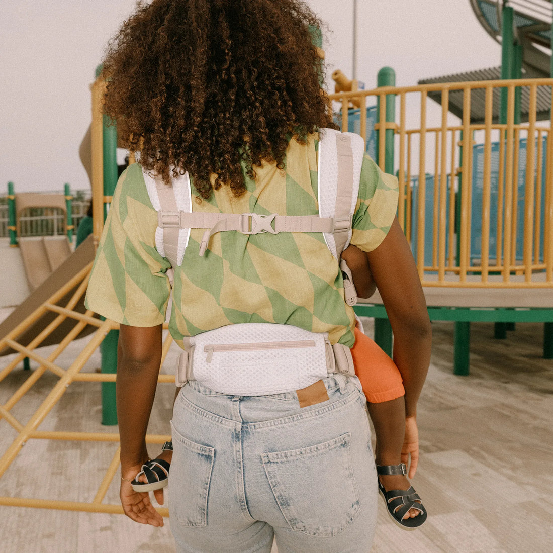 Back of a person holding a baby in a baby carrier at a playground