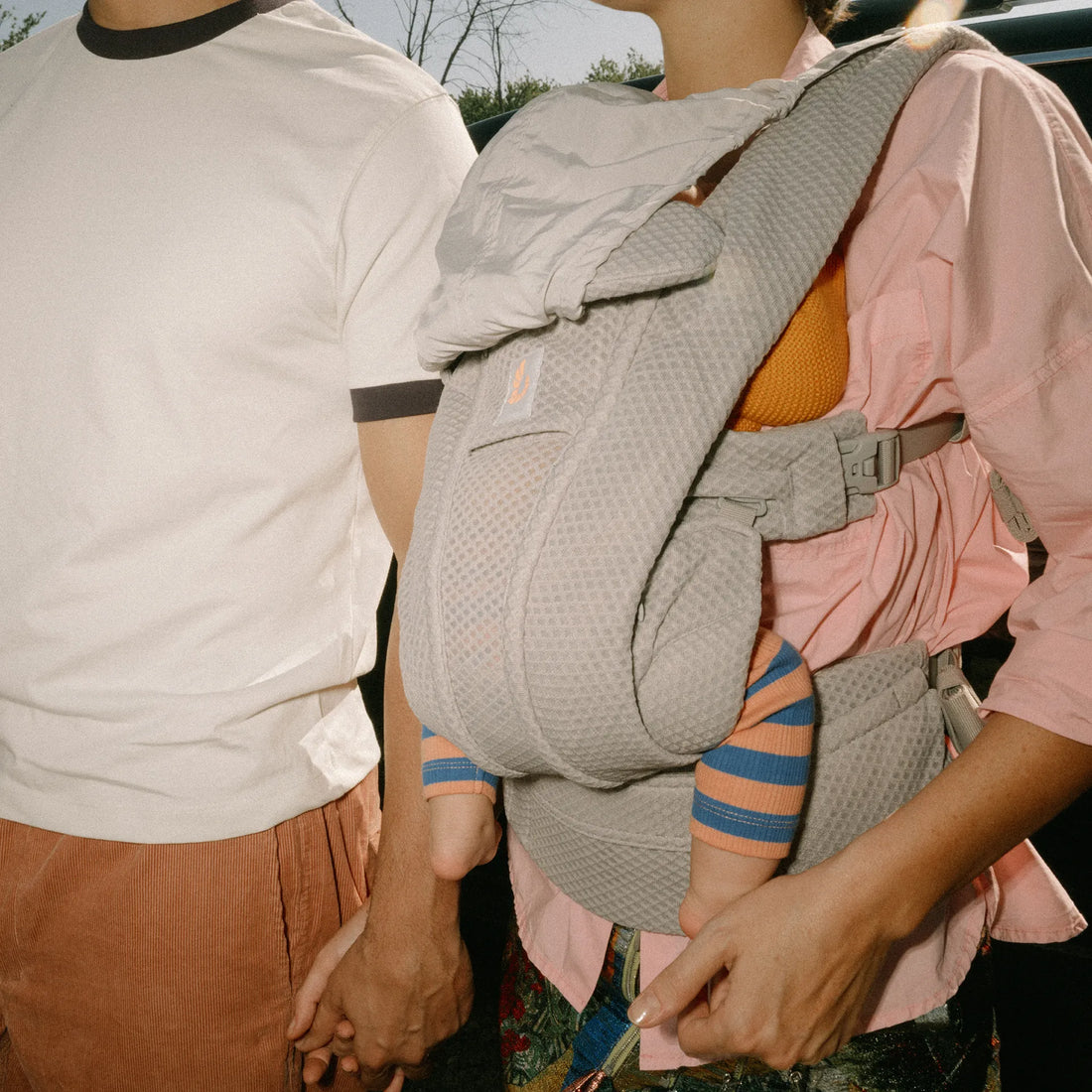 Woman holding a baby in a baby carrier and holding a mans hand