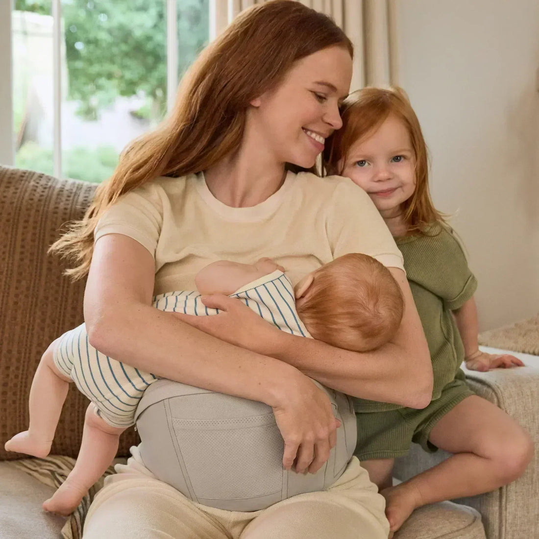 Woman breastfeeding a baby while sitting on a couch with another child beside her
