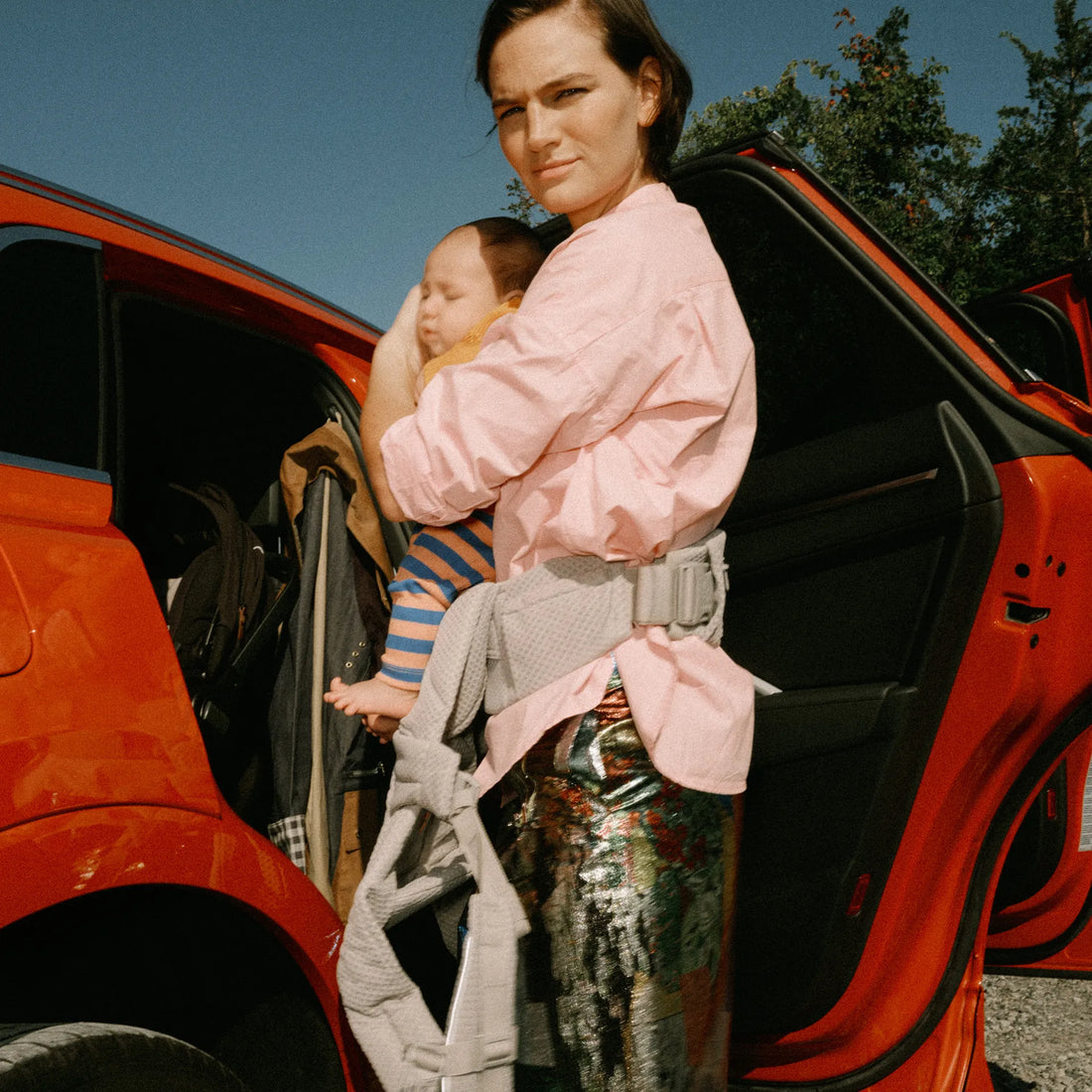Woman holding a baby in a baby carrier next to a car