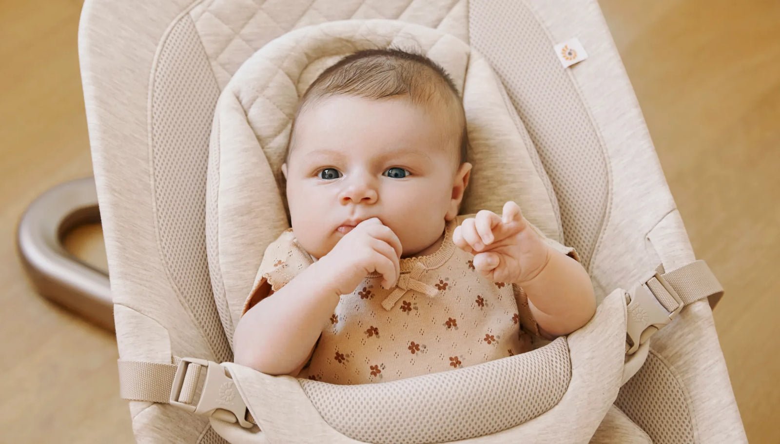 Baby sitting in a beige baby seat with a neutral background