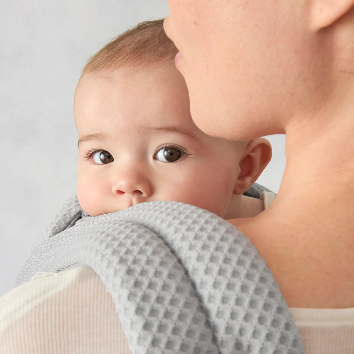 Baby being held by a person wearing a gray textured garment against a light background