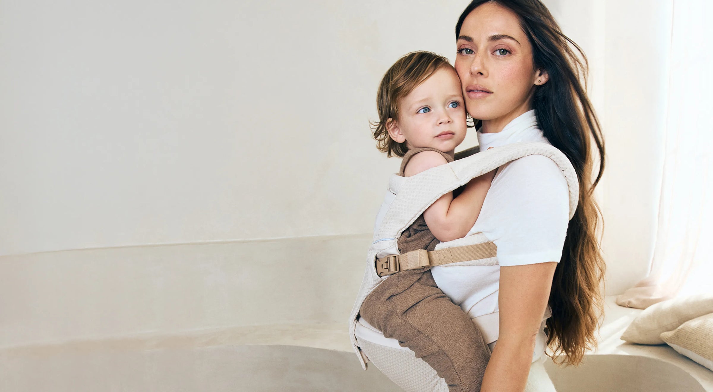 Woman holding a child in an ergobaby alta baby carrier against a white background