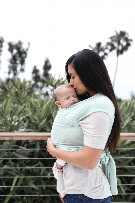 mom kissing baby's head as she holds him/her in ergobaby aura baby wrap