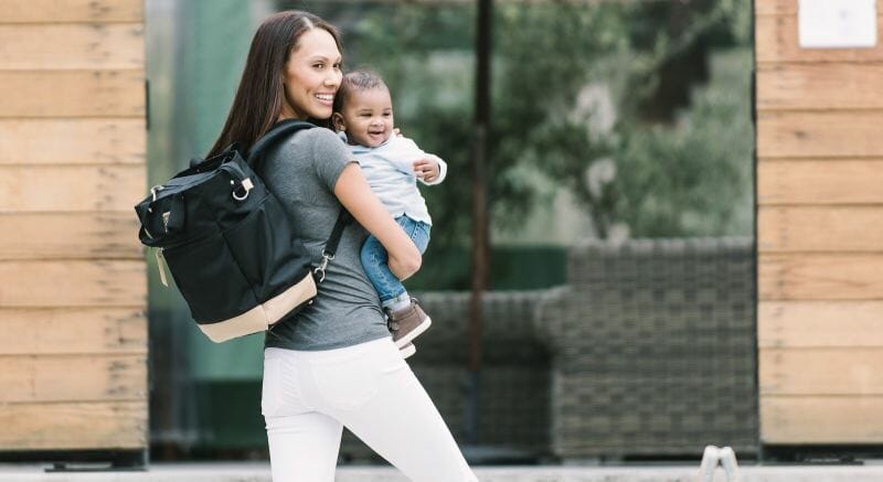 mom holding baby carrying ergobaby diaper bag