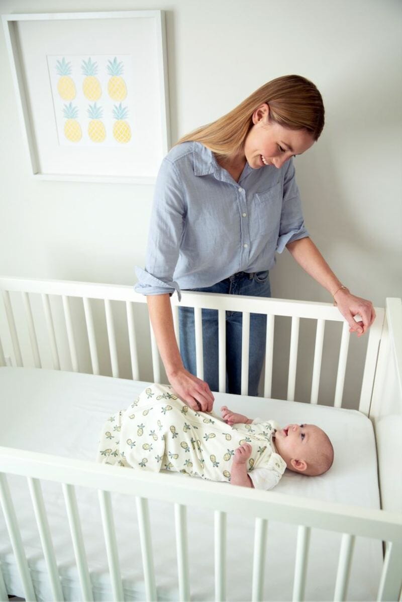 mom looking at sleeping baby in crib in ergobaby swaddler