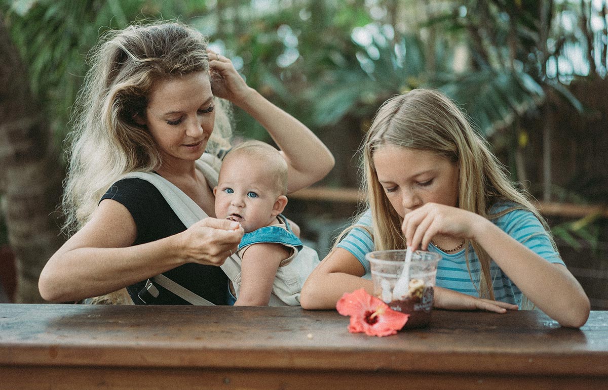 Mom giving baby a spoonful of food while in baby carrier